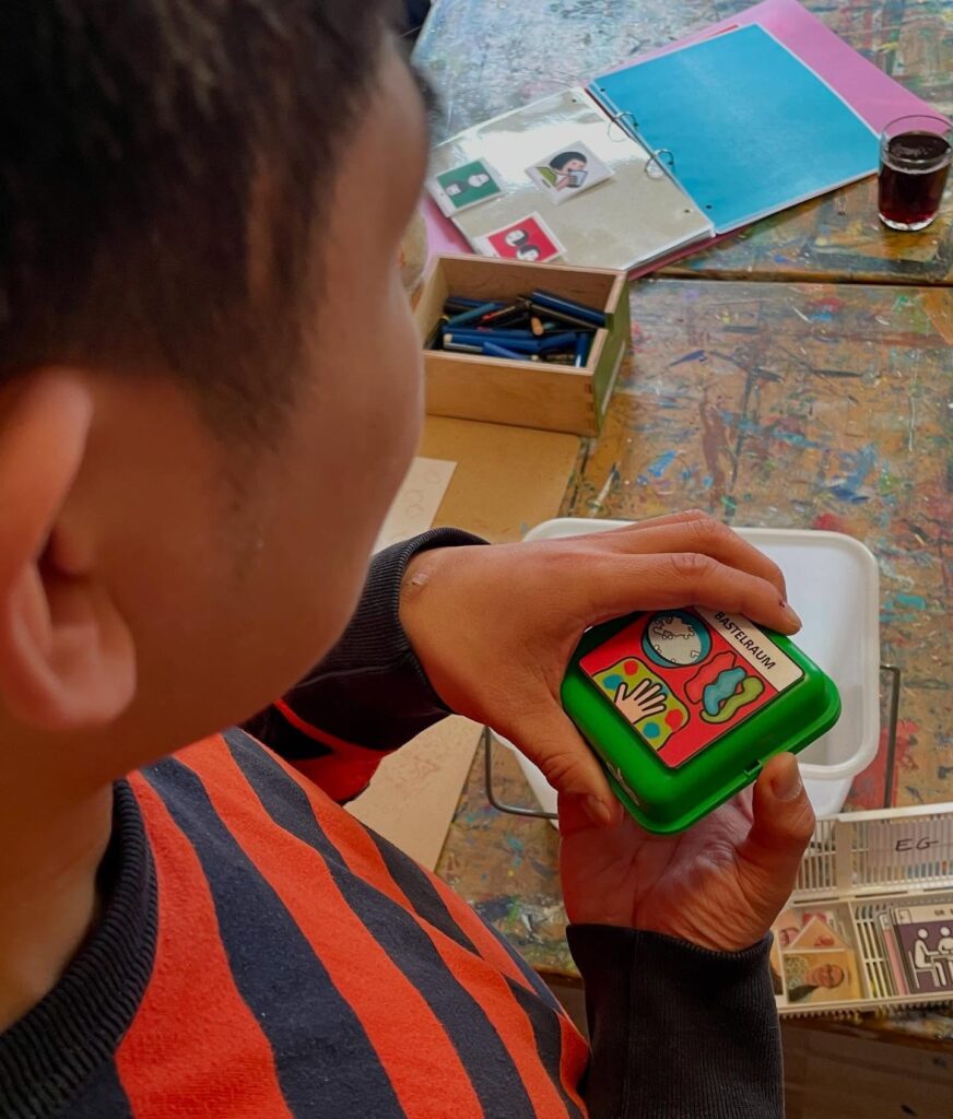 Ein Klient arbeitet mit einem grünem Sprechtaster, auf diesem ist ein Piktogramm vom Bastelraum.