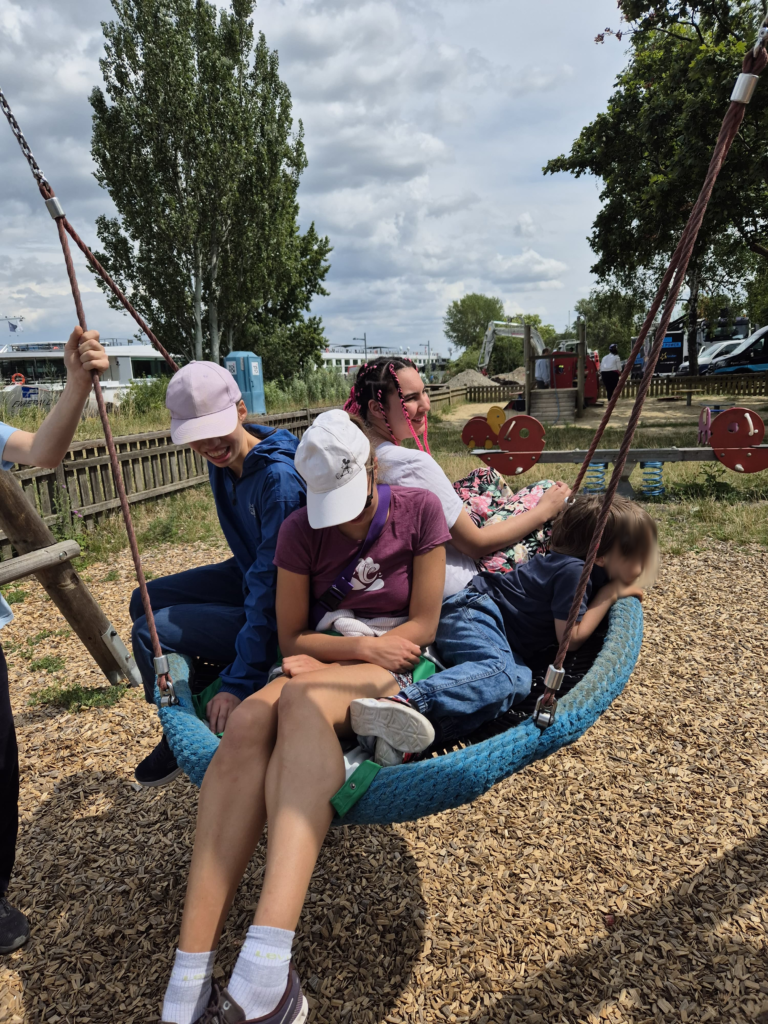 Klientinnen beim schaukeln in einer Korbschaukel am Spielplatz.