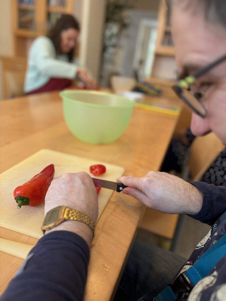 Ein Klient der Haushaltsgruppe beim schneiden von Paprika.