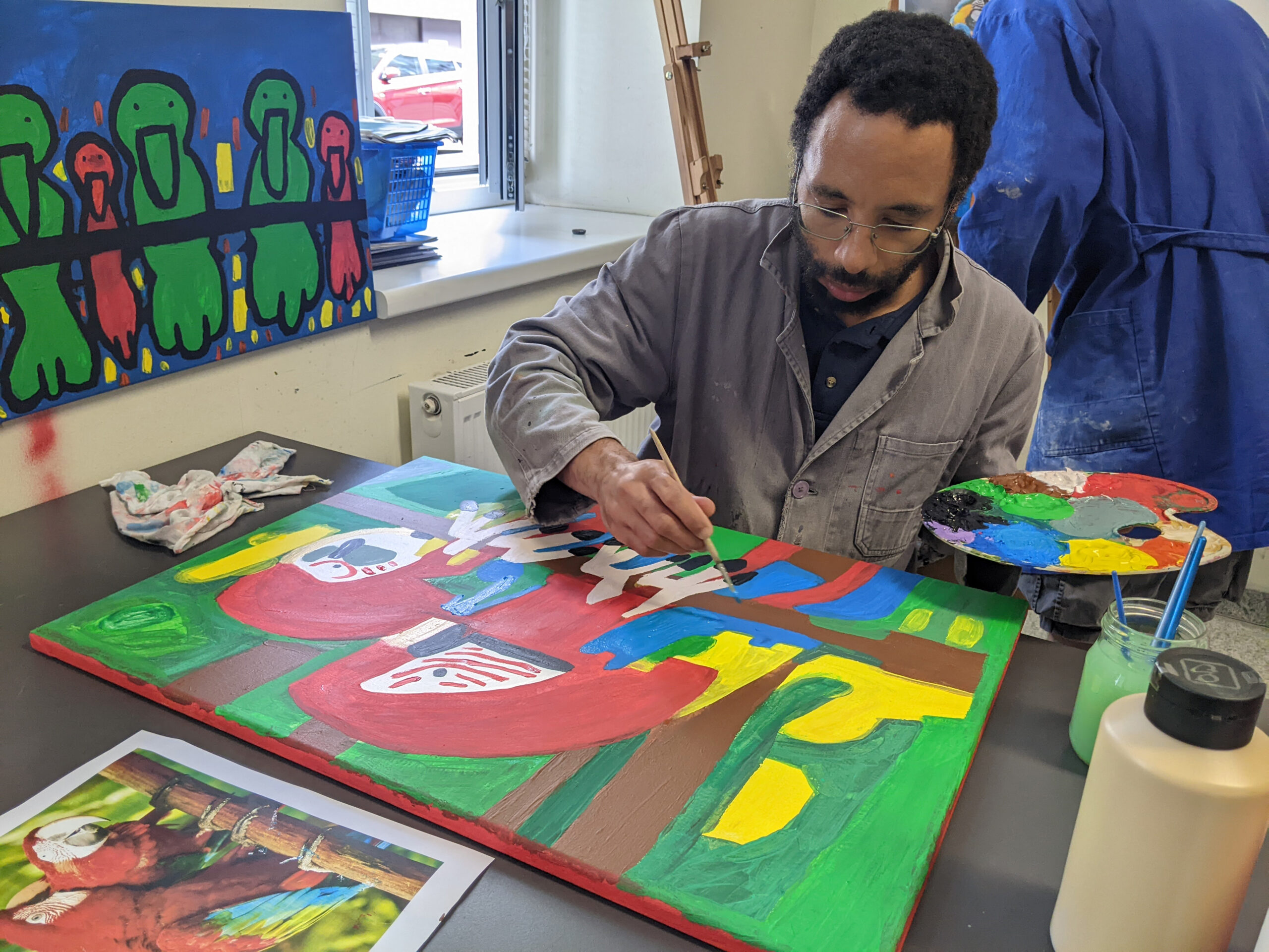 Klient der Künstlergruppe malt ein Papageienbild mit Acrylfarben.